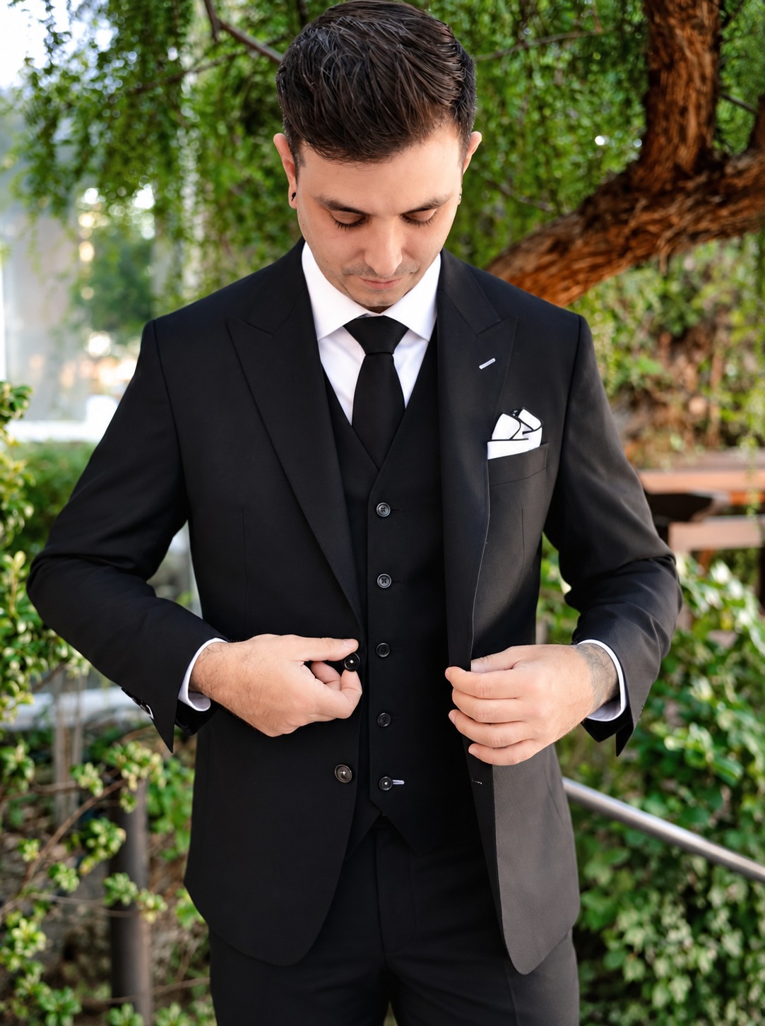 Groom fastening a custom black three-piece wedding suit with a matching waistcoat